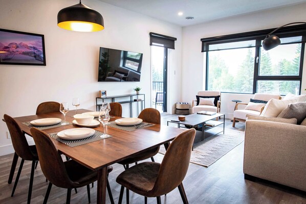 Un salon moderne comprenant un coin repas, de grandes fenêtres et un téléviseur à écran plat.