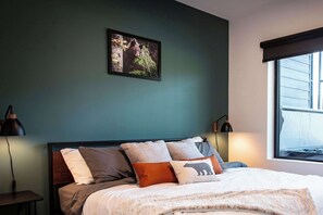 A bedroom with a bed, a nightstand, a lamp, a window, and a framed picture on the wall. - The Three Bear Penthouse - with Hot Tub (Revelstoke)