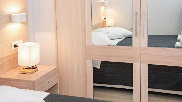 Een moderne hotelkamer met een bed, nachtkastje, lamp, kledingkast en een spiegel die het bed weerspiegelt.