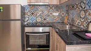 Een keuken met een roestvrijstalen koelkast, een inbouwoven, een spoelbak en een spatwand met kleurrijke tegels.