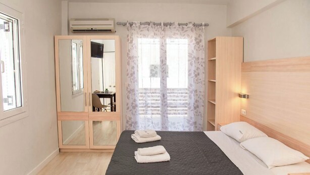 Un dormitorio con cama, armario, espejo, escritorio y ventana con cortinas.