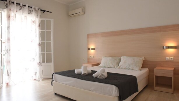 A bedroom with a bed, bedside tables, a nightstand, an air conditioning unit, and a window with curtains. - Antonias Iris apartment (Corfu)