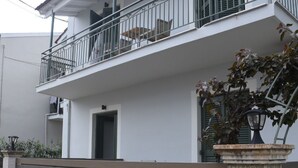 A two-story building with a balcony, a door, and a stone pillar. - Antonias Iris apartment (Corfu)