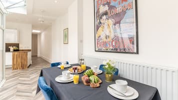 A dining area with a table set for breakfast, including fruits and beverages, and a poster on the wall.