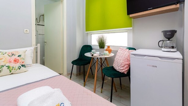A compact room with a bed, a small table with a plant, two chairs, a coffee maker, and a television. - Theodora's Nest - air coditioning, located in the heart of Corfu old city (Corfu)