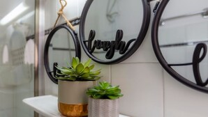 A bathroom with a white tiled wall, two potted plants on a shelf, and a mirror with the word "laugh" on it. - Theodora's Nest - air coditioning, located in the heart of Corfu old city (Corfu)
