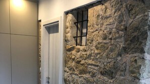 Um quarto com parede de pedra, uma porta e um candeeiro.