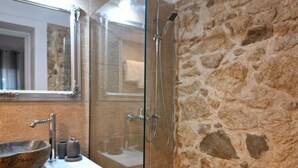 Casa de banho com parede de pedra, cabine de duche com vidro, lavatório grande em forma de tigela e espelho.