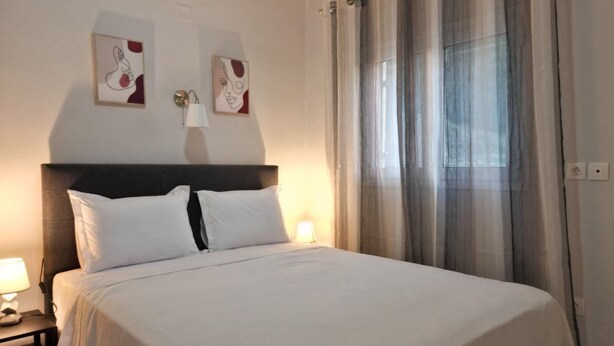 Quarto de hotel com uma cama grande, duas luminárias de cabeceira e uma janela com cortinas finas.