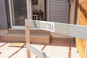 A wooden bench with the word "ELECTRA" on it, placed outside a house with a door and steps leading to a porch.