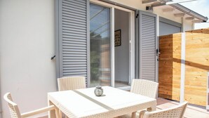 Une terrasse avec une table et des chaises en osier blanc, une clôture en bois et une porte-fenêtre coulissante.