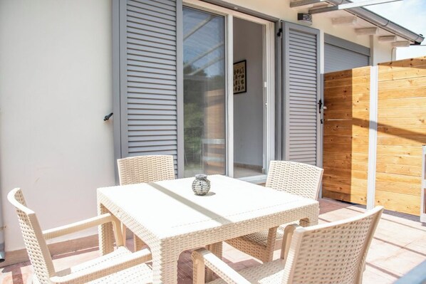A patio with a white wicker table and chairs, a wooden fence, and a sliding glass door.
