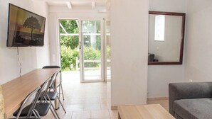 Une pièce comprenant une table en bois, des chaises, un canapé, un téléviseur et une porte-fenêtre coulissante donnant sur un balcon.