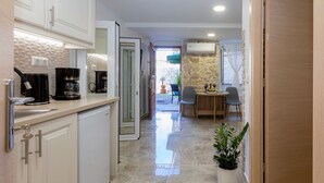 A modern kitchen with white cabinets, a coffee machine, and a dining area with a table and chairs. - Volto Achilles Suite (Corfu)