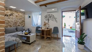 Ein gemütliches Wohnzimmer mit Steinwand, Holzboden und einem Essbereich mit Tisch und Stühlen. Ein Fernseher ist an der Wand befestigt.