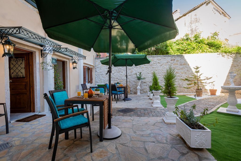 An outdoor patio with stone flooring, a table with chairs, and a large green umbrella.