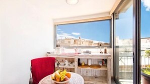 Een balkon met uitzicht op gebouwen, een klein tafeltje met een schaal fruit en een rode handdoek.