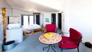 Een kleine hotelkamer met een bed, een tafeltje met een banaan en twee rode stoelen.