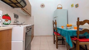 A compact kitchen with a stove, sink, and a dining area with a table and chairs. - Campiello Blue Studio - Central cozy studio with garden in Corfu old town (Corfu)