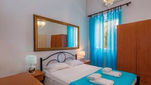 A hotel room with a bed, a nightstand, a wooden wardrobe, and a large mirror on the wall. - Campiello Blue Studio - Central cozy studio with garden in Corfu old town (Corfu)