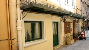 A narrow street with a building featuring a green door and window, a balcony with a railing, and a scooter parked outside. - Conte Studio - located in the heart of Corfu Old town (Kerkira)