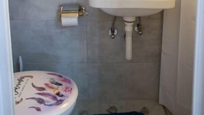 A small bathroom with a toilet, sink, and mirror. - Conte Studio - located in the heart of Corfu Old town (Kerkira)