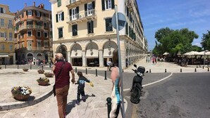 A public square with buildings, a fountain, and a parked motorcycle. - Pento Studio - Ground floor apt, located near Corfu square (Kerkira)