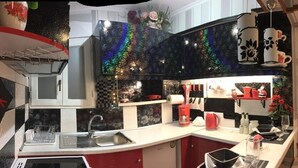 A kitchen with a modern design, featuring a black backsplash, white cabinets, and a red countertop. There is a sink, a stove, and various kitchen appliances. - Pento Studio - Ground floor apt, located near Corfu square (Kerkira)