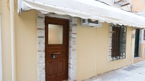 A building with a brown door, stone facade, and a white awning. - Pento Studio - Ground floor apt, located near Corfu square (Kerkira)