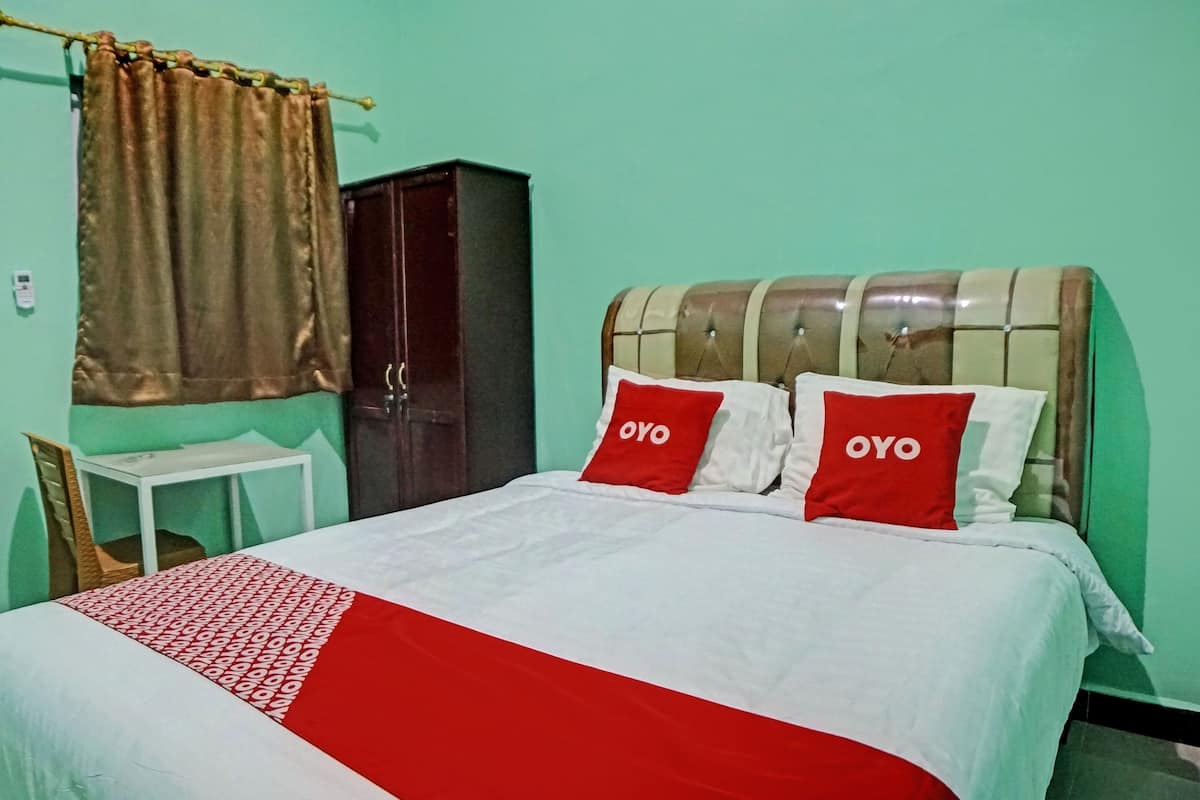 Ein Bett mit zwei OYO-Kissen, einer weiß-roten Bettdecke, einem braunen Vorhang, einem weißen Tisch und einem dunkelbraunen Kleiderschrank.