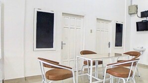 Un salón de conferencias con una mesa rectangular y seis sillas marrones de estructura metálica. Hay dos puertas blancas con paneles de vidrio y un televisor instalado en la pared.