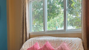 A room with a sofa covered in a patterned fabric, a window with curtains, and a view of trees outside. - Rang Noknoy Resort at Koh Larn (Koh Lan)