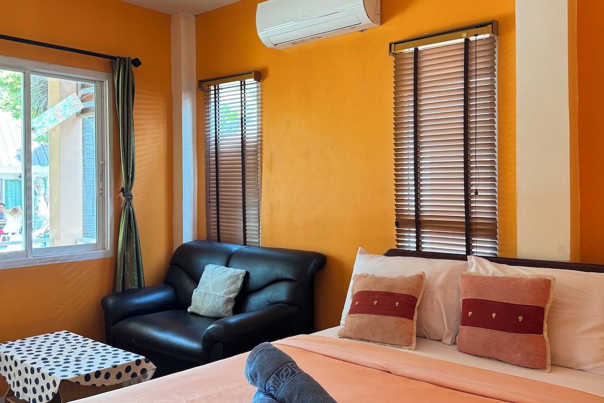 Quarto de hotel com cama, uma poltrona de couro preta, uma mesinha e uma janela com persianas.