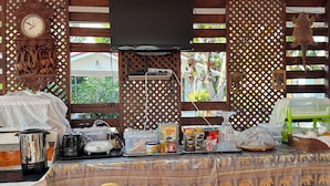 A kitchen area with a wooden table, a clock, and various kitchen appliances and utensils. - Rang Noknoy Resort at Koh Larn (Koh Lan)