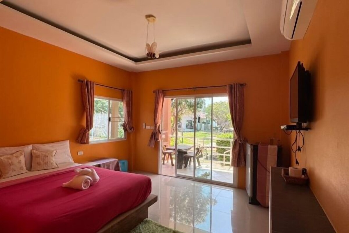 A hotel room with a bed, a TV, a window with curtains, and a sliding glass door leading to an outdoor area.