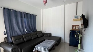 A modern living room with a black leather sofa, a checkered ottoman, a ceiling fan, and a small refrigerator. - Rang Noknoy Resort at Koh Larn (Koh Lan)