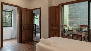 Een kamer met een bed, houten deuren, een raam en uitzicht op een balkon met tuinmeubilair.