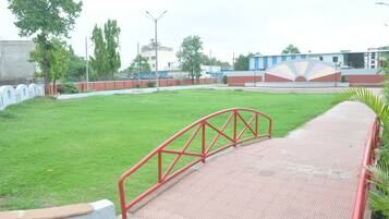 Stroll along the paved walkway to a serene grassy field surrounded by a low wall and trees.