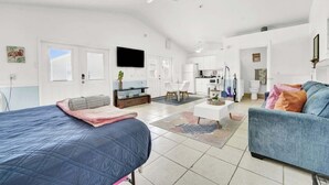 Un salón amplio con una cama grande, un sofá, una mesa de centro y un televisor. Se observa una cocina al fondo.