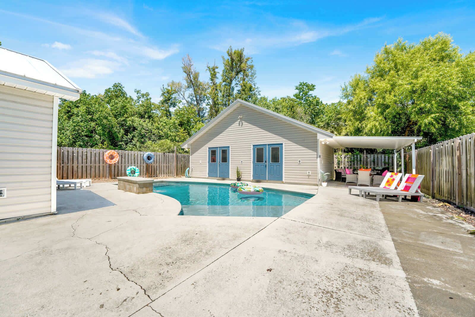 Ein Garten mit Schwimmbad, überdachter Terrasse und Holzzaun.