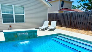 Una piscina con dos sillas reclinables blancas y una cerca de madera al fondo.