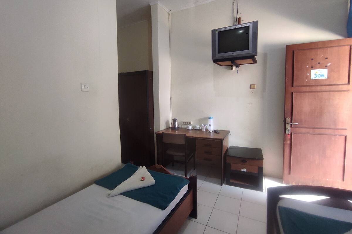 A small, simple room with a bed, a desk, a chair, and a television mounted on the wall.