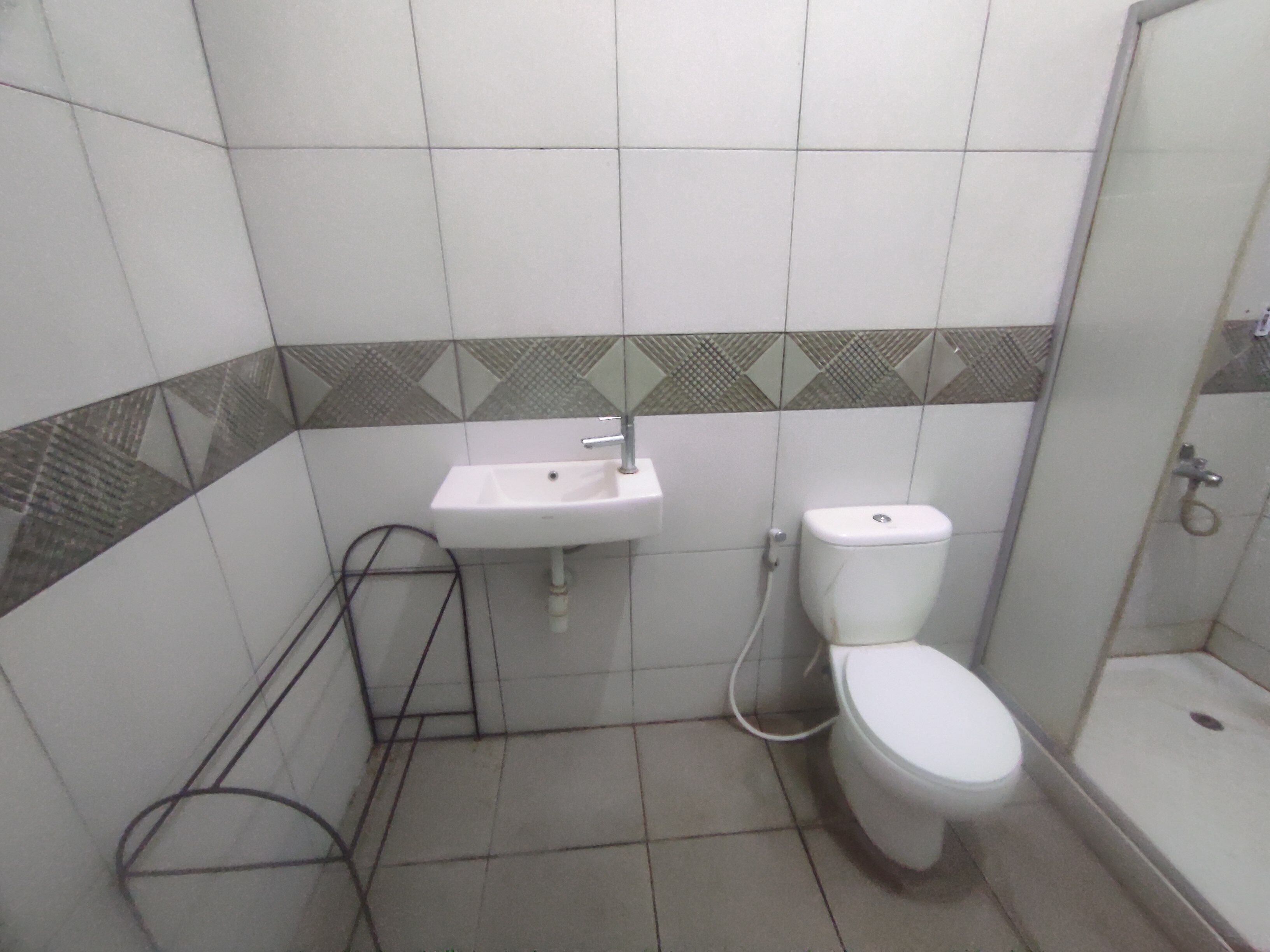 Ein kleines Badezimmer mit einem weißen Waschbecken, einer Toilette und einer Dusche. Die Wände sind im unteren Bereich mit einem geometrischen Muster geflieselt.