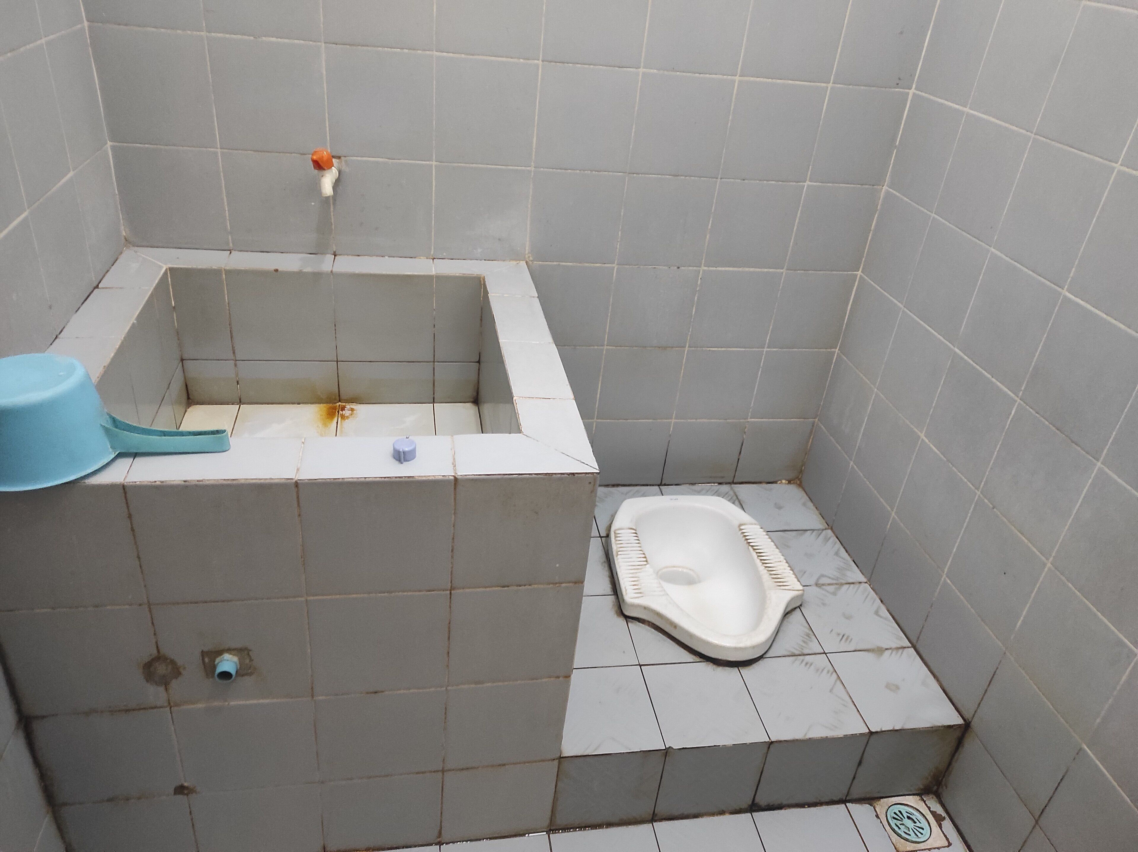 A small, tiled bathroom with a bathtub, toilet, and a blue basin.