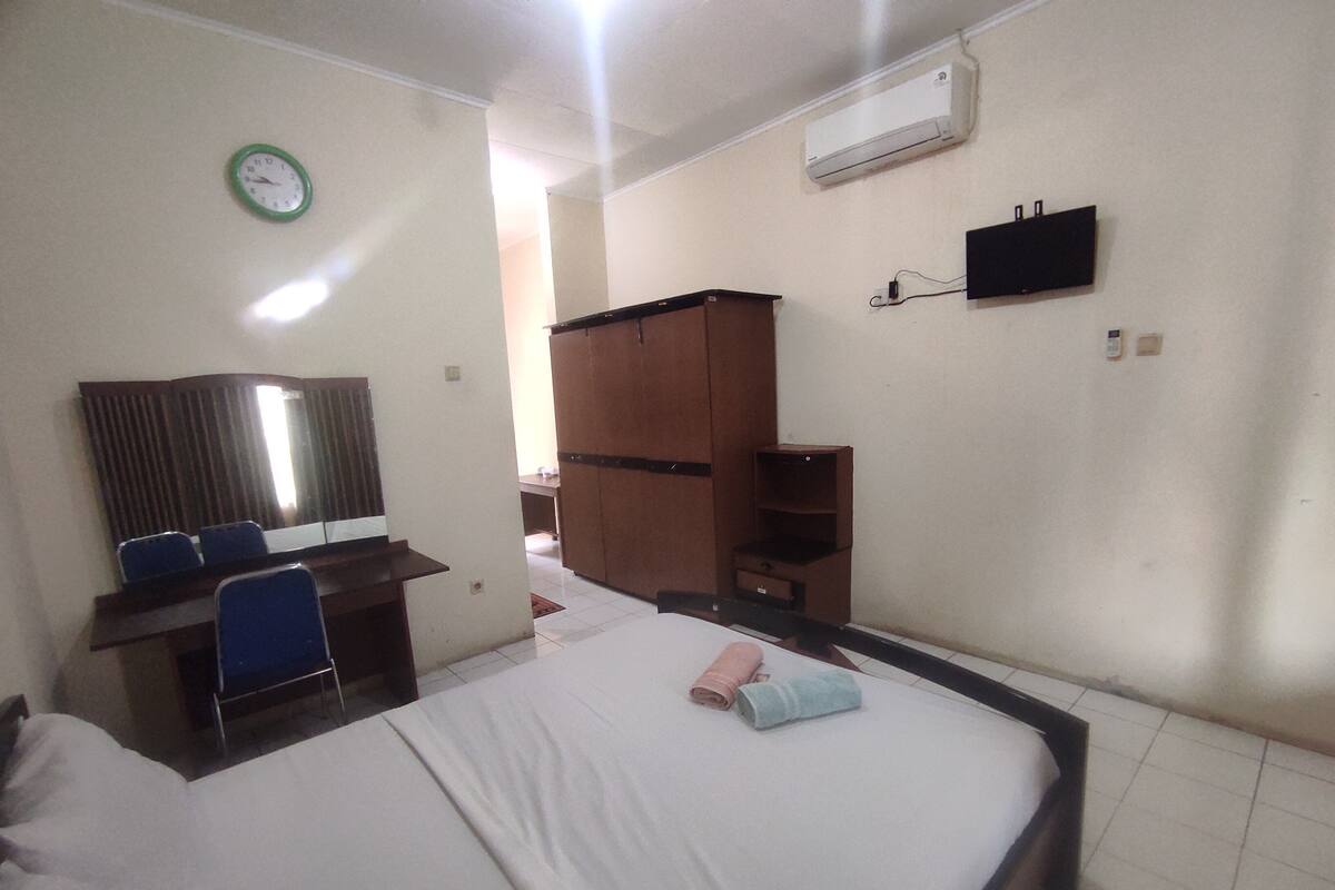A hotel room with a bed, a desk with a chair, a wardrobe, and a wall-mounted TV.