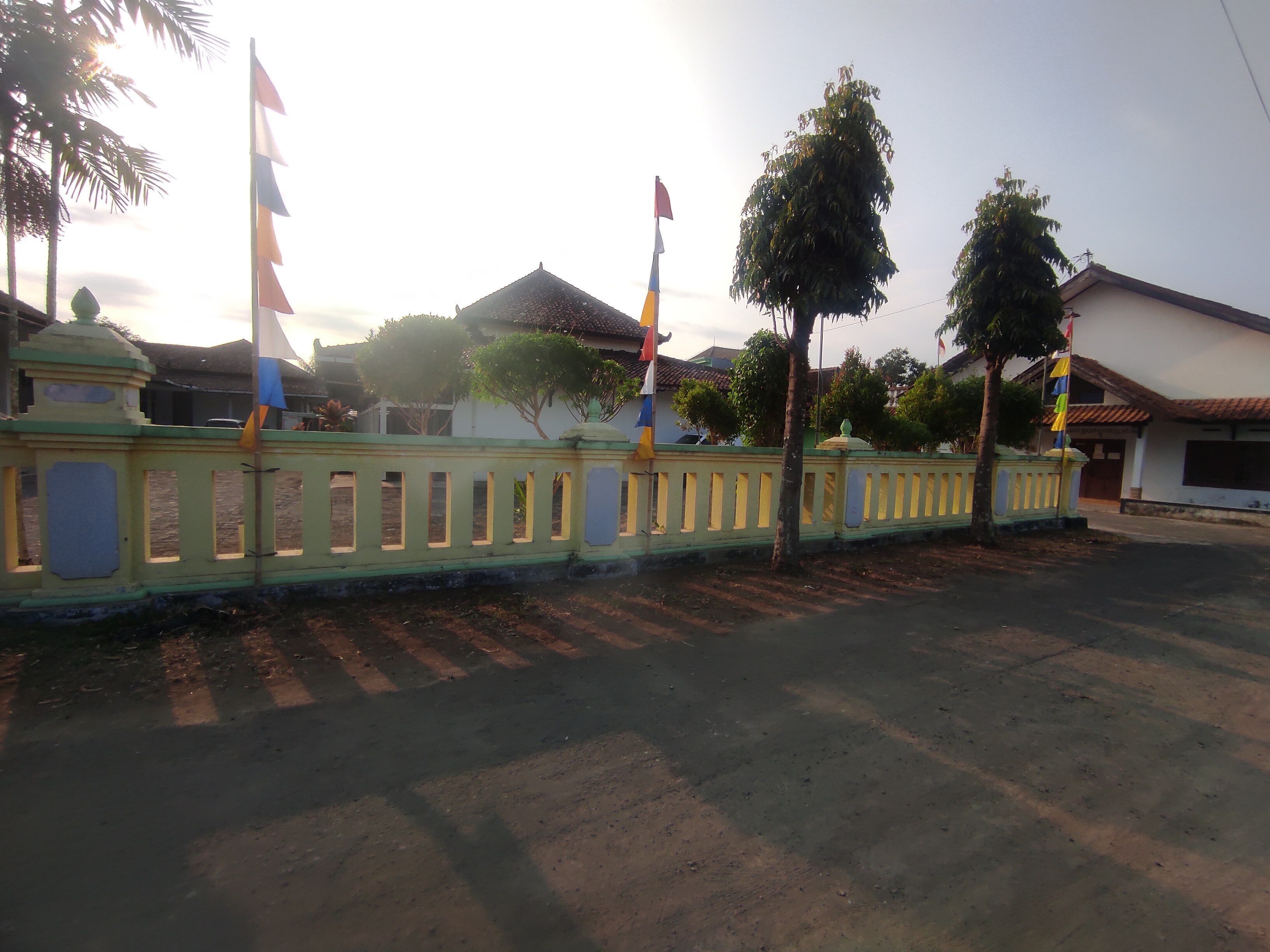 A gated area with multiple flags, a paved road, and a building with a tiled roof.