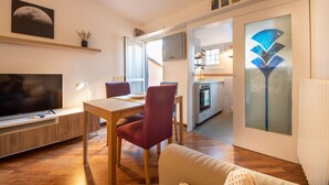 A modern living room with a TV, dining table, and red chairs. A kitchen is visible through an open door. - HouSmart Tovaglie 9 int. 6 (Bologna)