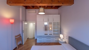 A bedroom with a wooden ceiling, white wardrobe, bedside table with lamp, and a wooden chair. - HouSmart Tovaglie 9 int. 6 (Bologna)
