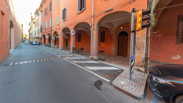 A narrow street with buildings on either side, featuring arched doorways and a pedestrian crossing. - HouSmart Tovaglie 9 int. 6 (Bologna)