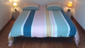 A bedroom with a bed, two bedside tables, and a lamp on each table. - Gite Coriosolites (Quemper-Guézennec)
